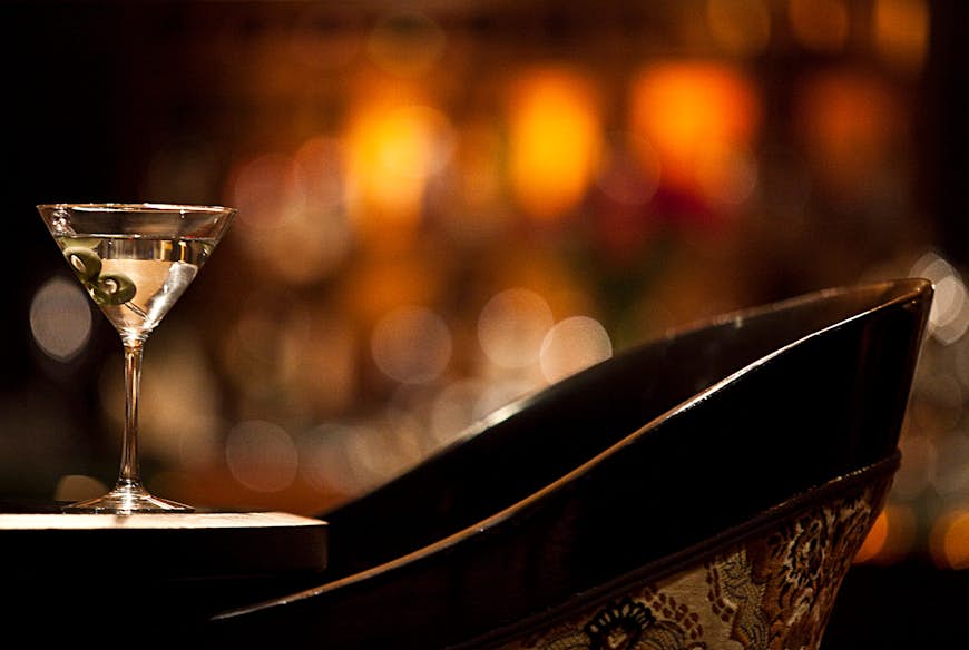 A martini glass filled with clear liquid and two green olives stands on a table at Rick's bar in the Taj Mahal Hotel