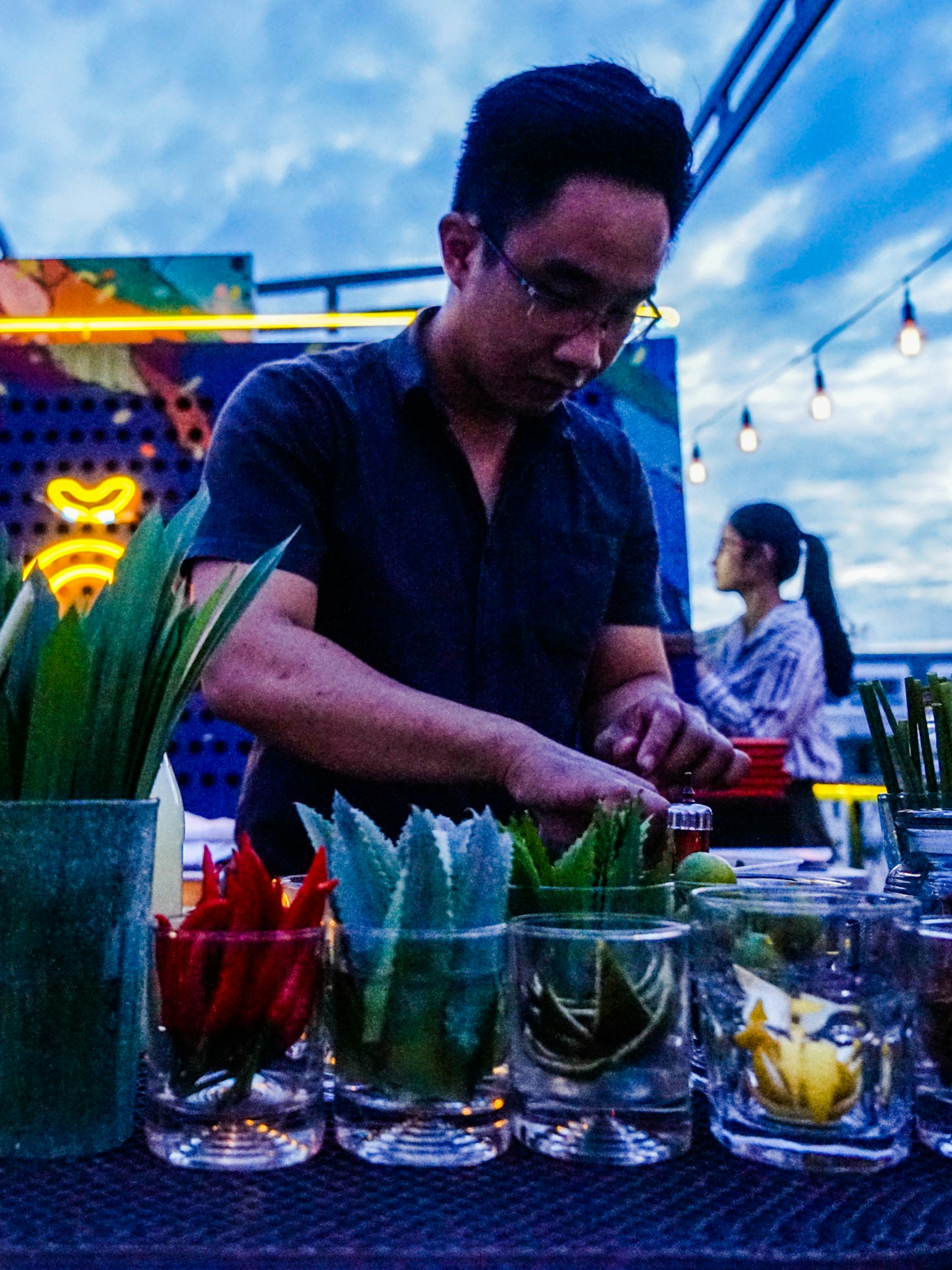 A barman mixes a 'phojito' at Anan at dusk, one of HCMC's best rooftop bars. The bar counter is lined with containers of lemons, limes and various other cocktail ingredients. 