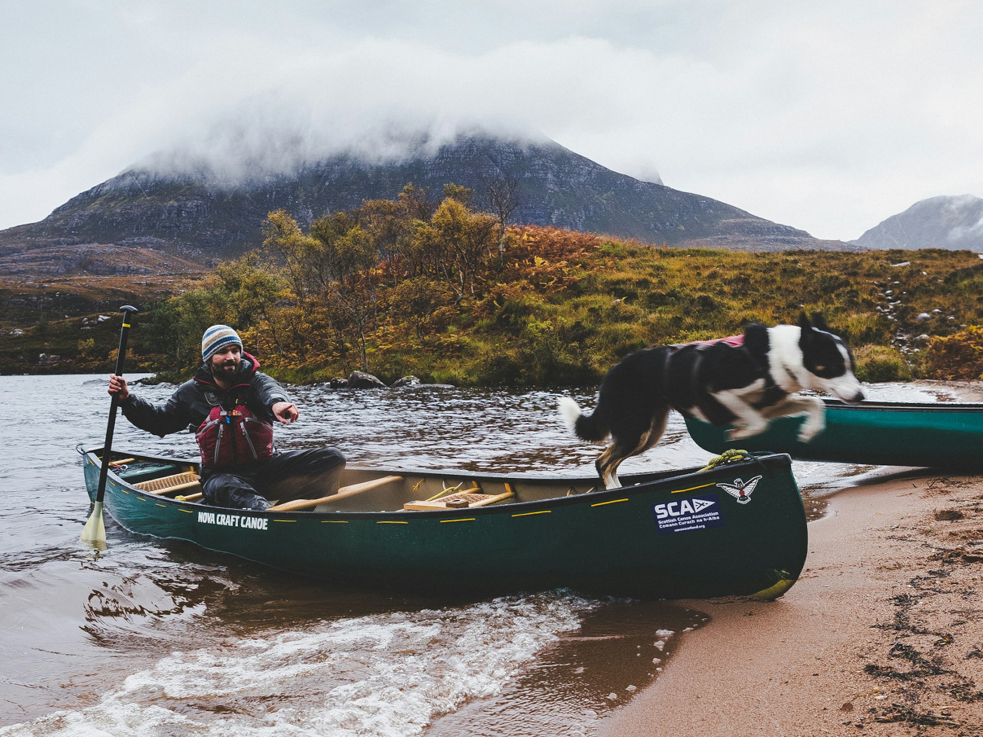 Kiera the border collie leaps out of a canoe as guide Tim Hamlet beaches it on Loch Lurgainn under the peak of Stac Pollaidh