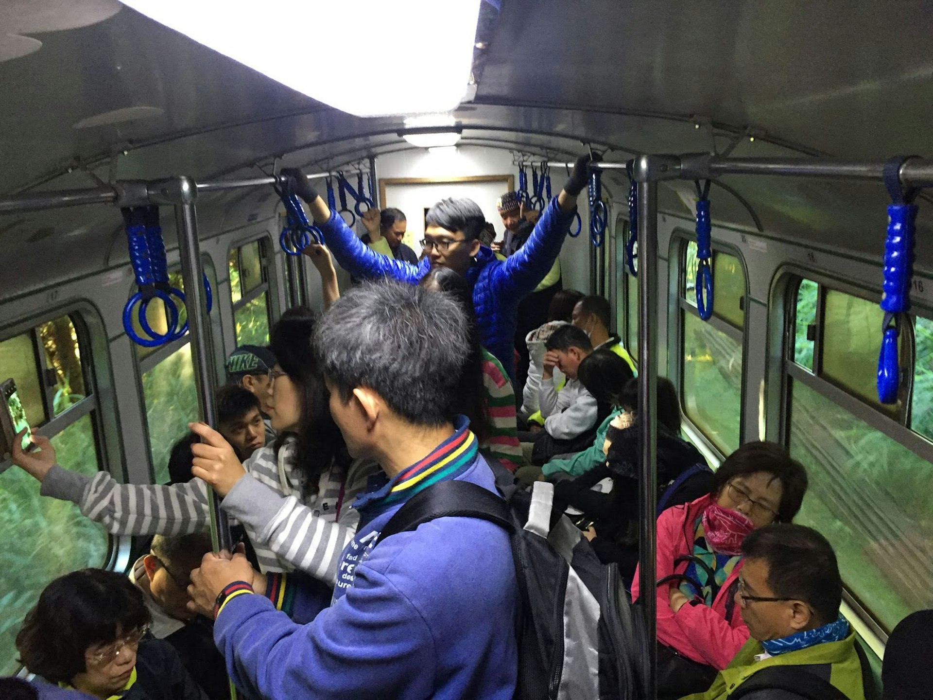 Visitors seated and standing, packed into a train carriage, some holding on to the railings. 