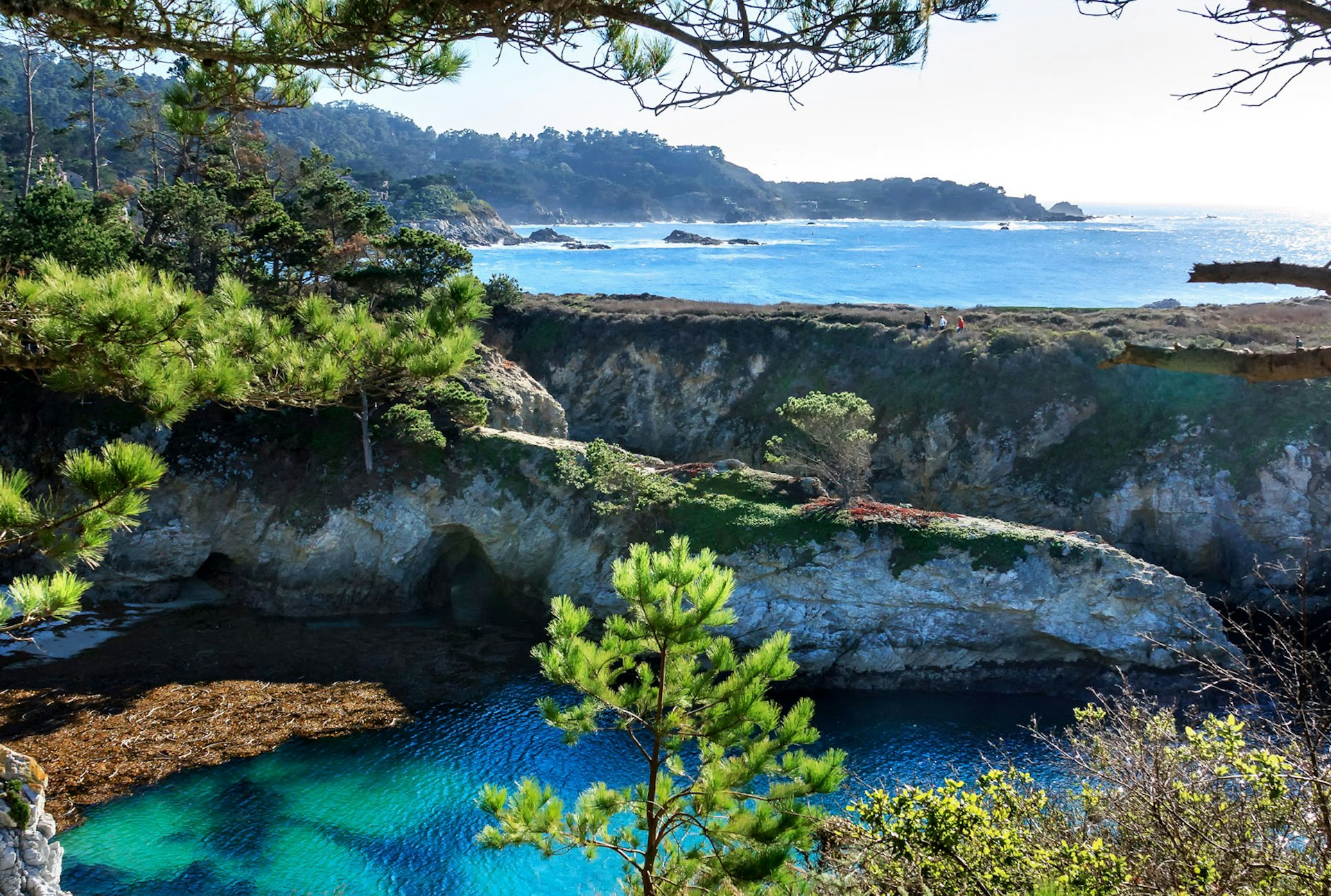 Three people walk the ridgeline between the pacific ocean and a protected cove with turqoise waters