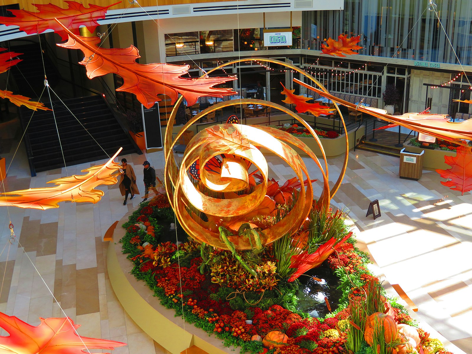 aerial view of a large-scale, copper spiral art piece, placed within a garden of orange, green and red plants 