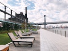 Lawn chairs line up along the waterfront with the Domino Sugar Factory in the background at Domino Park