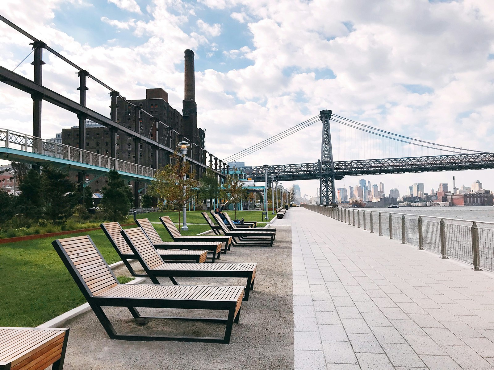 Lawn chairs line up along the waterfront with the Domino Sugar Factory in the background at Domino Park