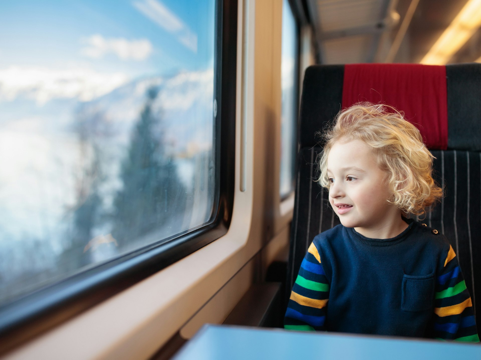 A smiling child of around five years old sits in a train seat looking out at a snowy landscape