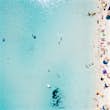 Aerial of a beach with tourists swimming in clear water and lounging on the sand.