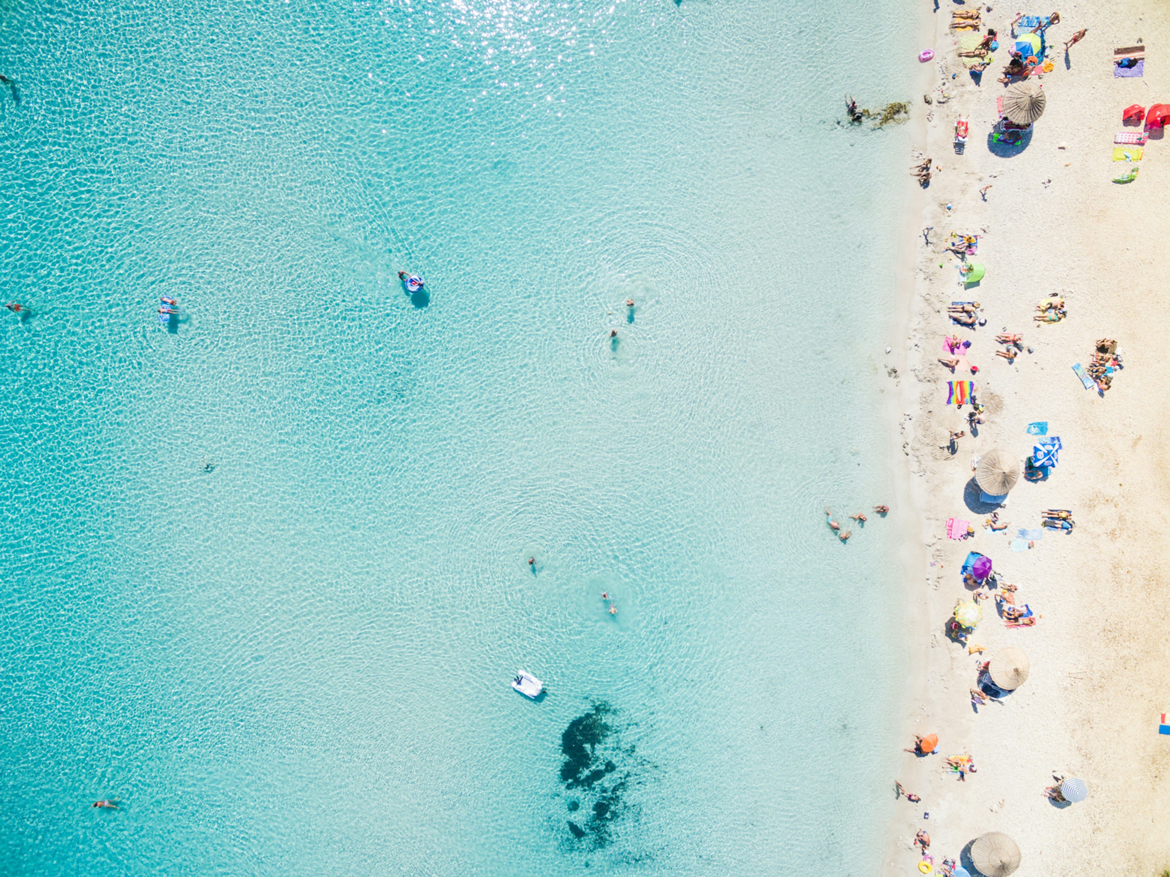 Aerial of a beach with tourists swimming in clear water and lounging on the sand.