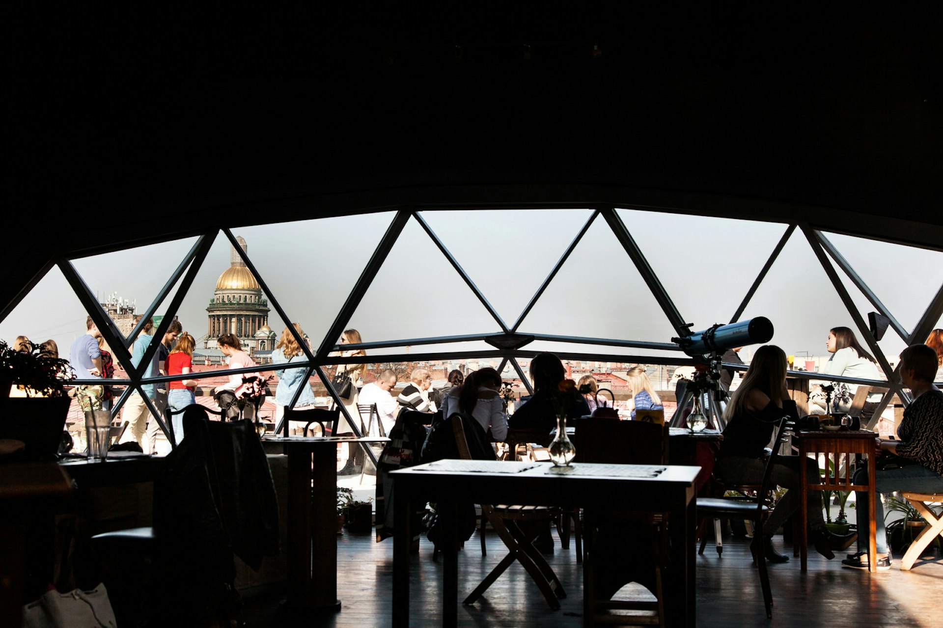 An interior of a rooftop cafe in St Peterburg, with a view of the city skyline through the windows