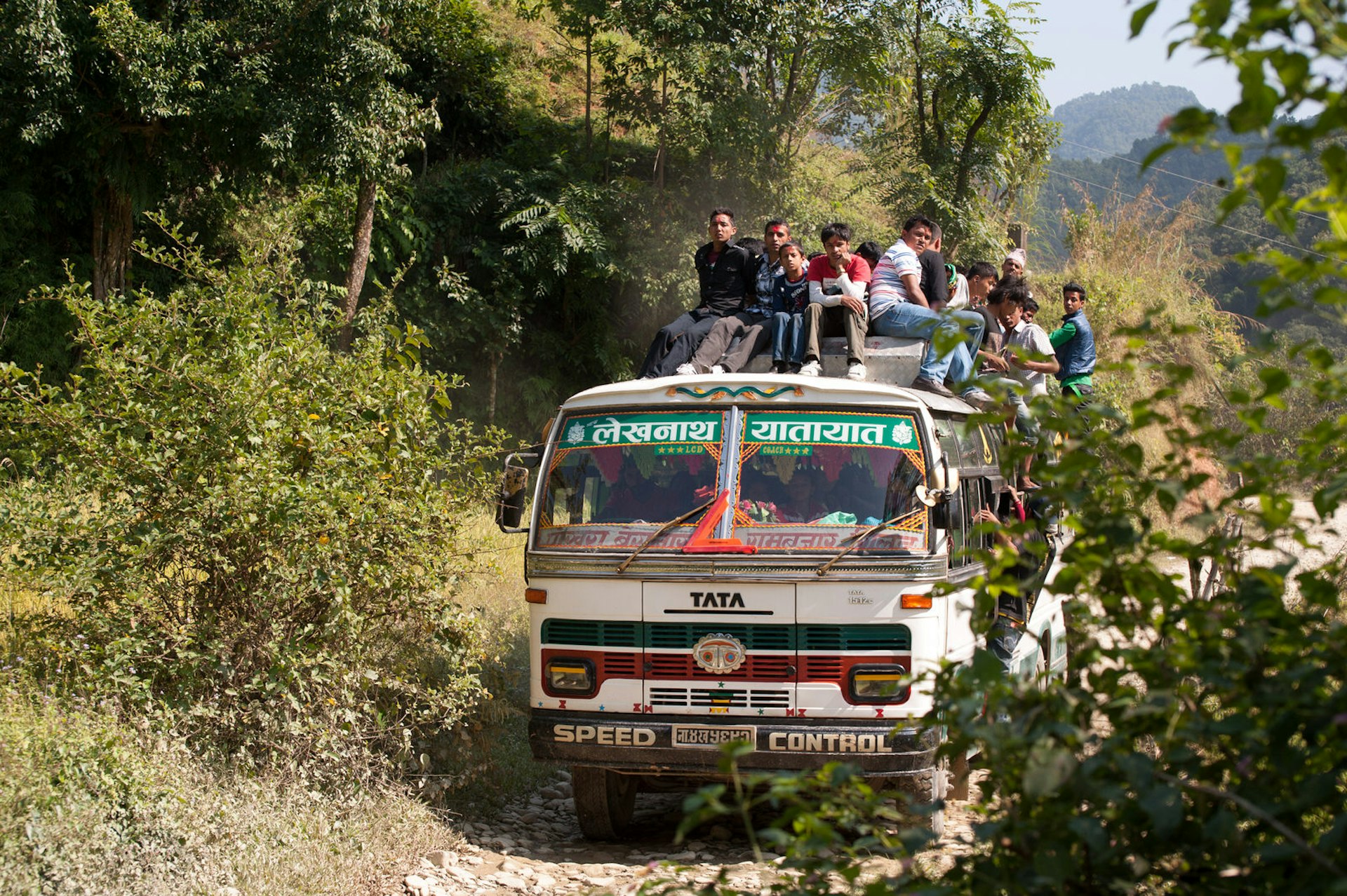 Passengers sitting on the roof of a bus travelling through rural Nepal