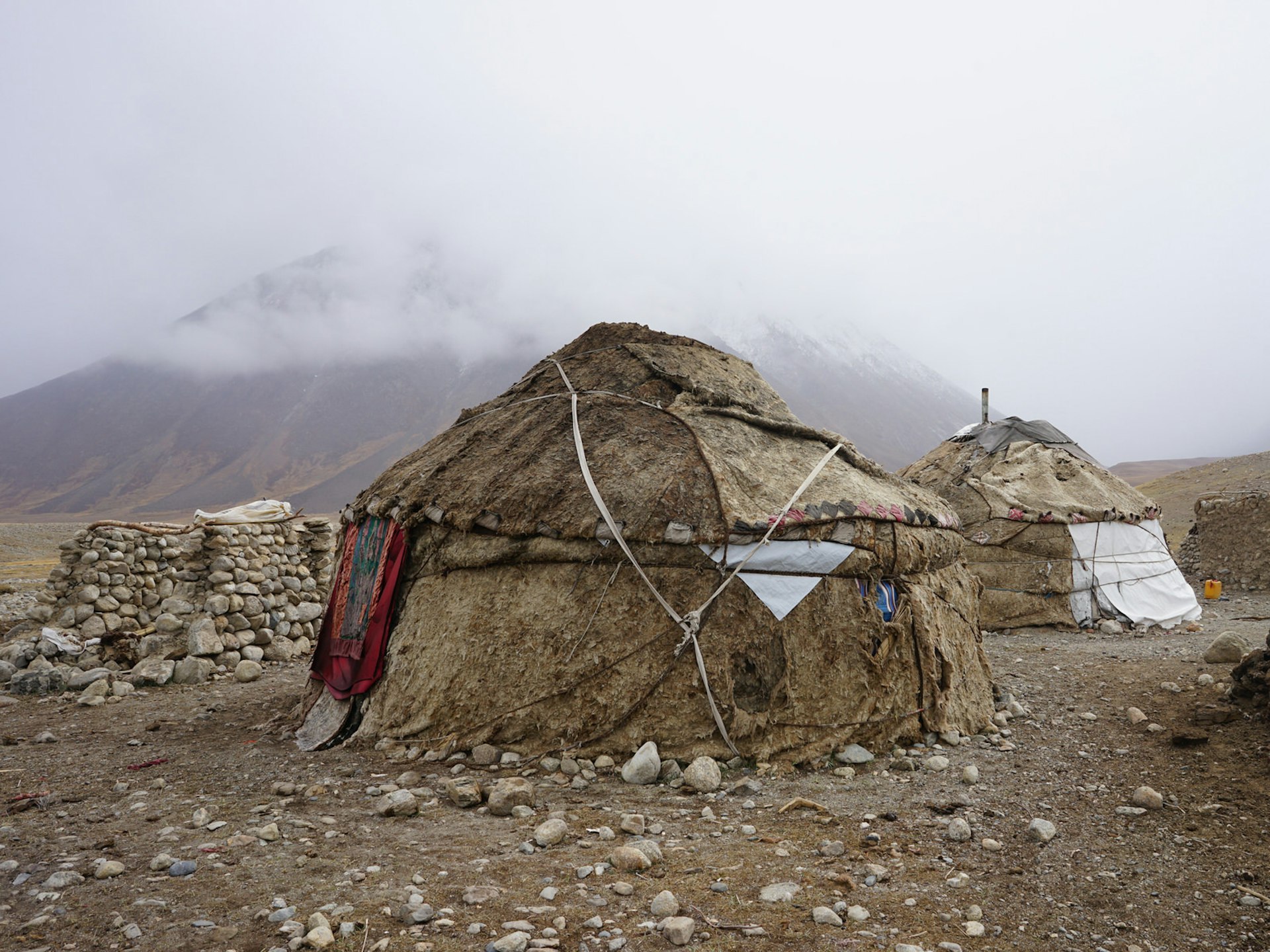 A traditional yurt tent camp made of wool and leather with mountains and fog in the background