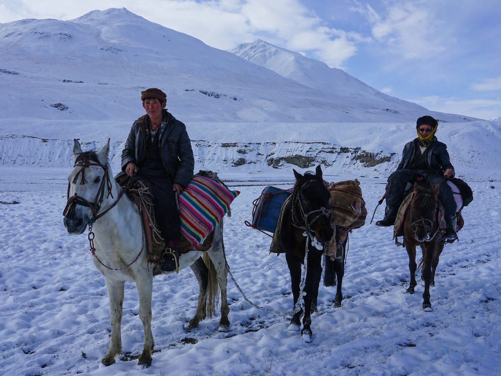 Two men on horses leading a donkey through a snowy mountain landscape