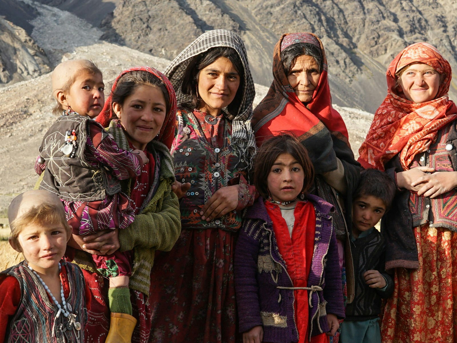 A Wakhan Kyrgyz family with grandmother, mothers and children, all dressed in traditional headscarves and colourful, embroidered clothing