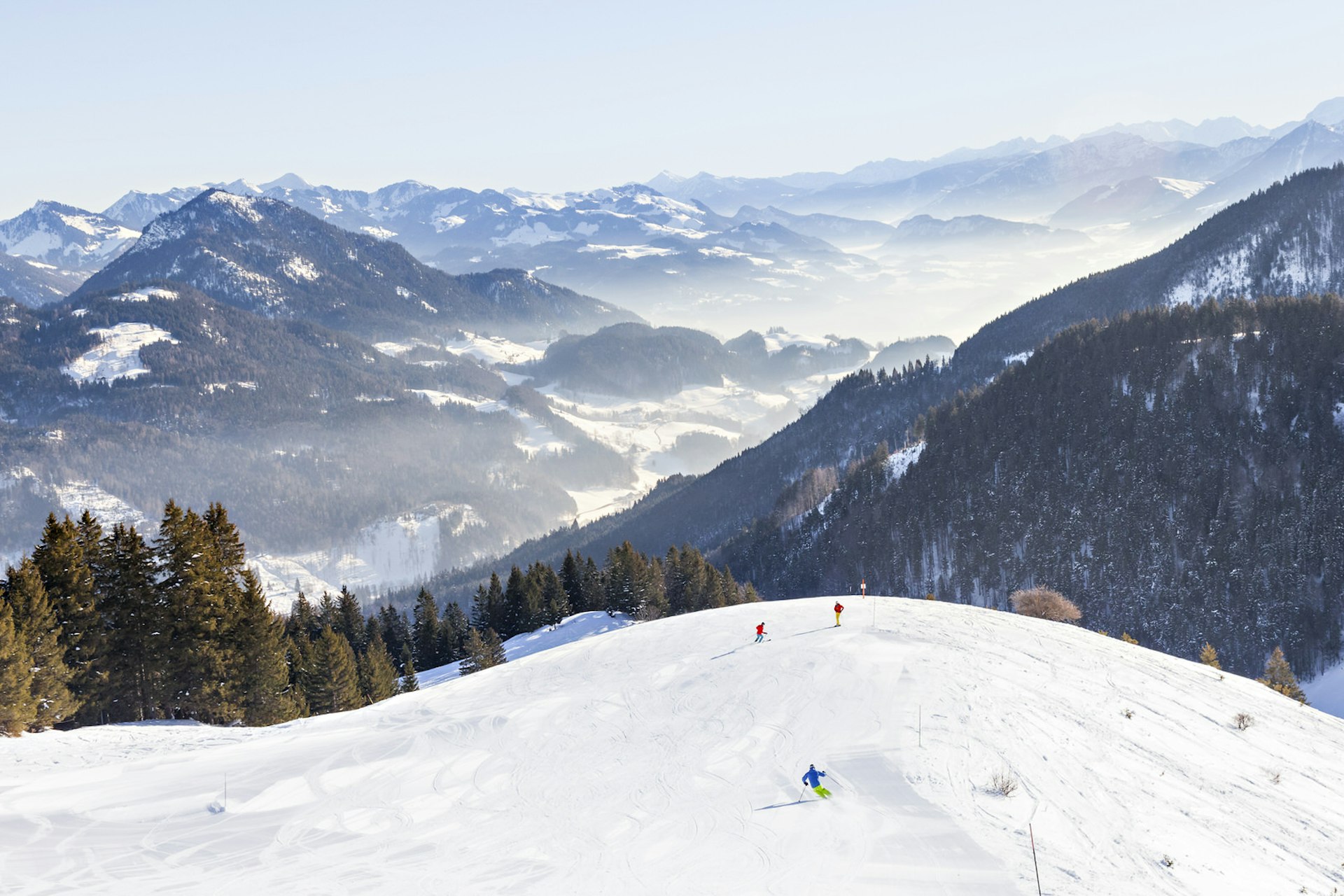 The top of a ski run at Sudelfeld–Bayrischzell ski resort, looking down over the snow-covered mountain range 