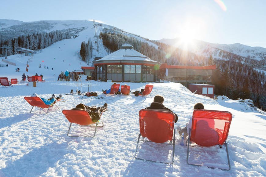Skiers and snowboarders taking a rest in chairs near an apres ski bar on the slopes of Jasna