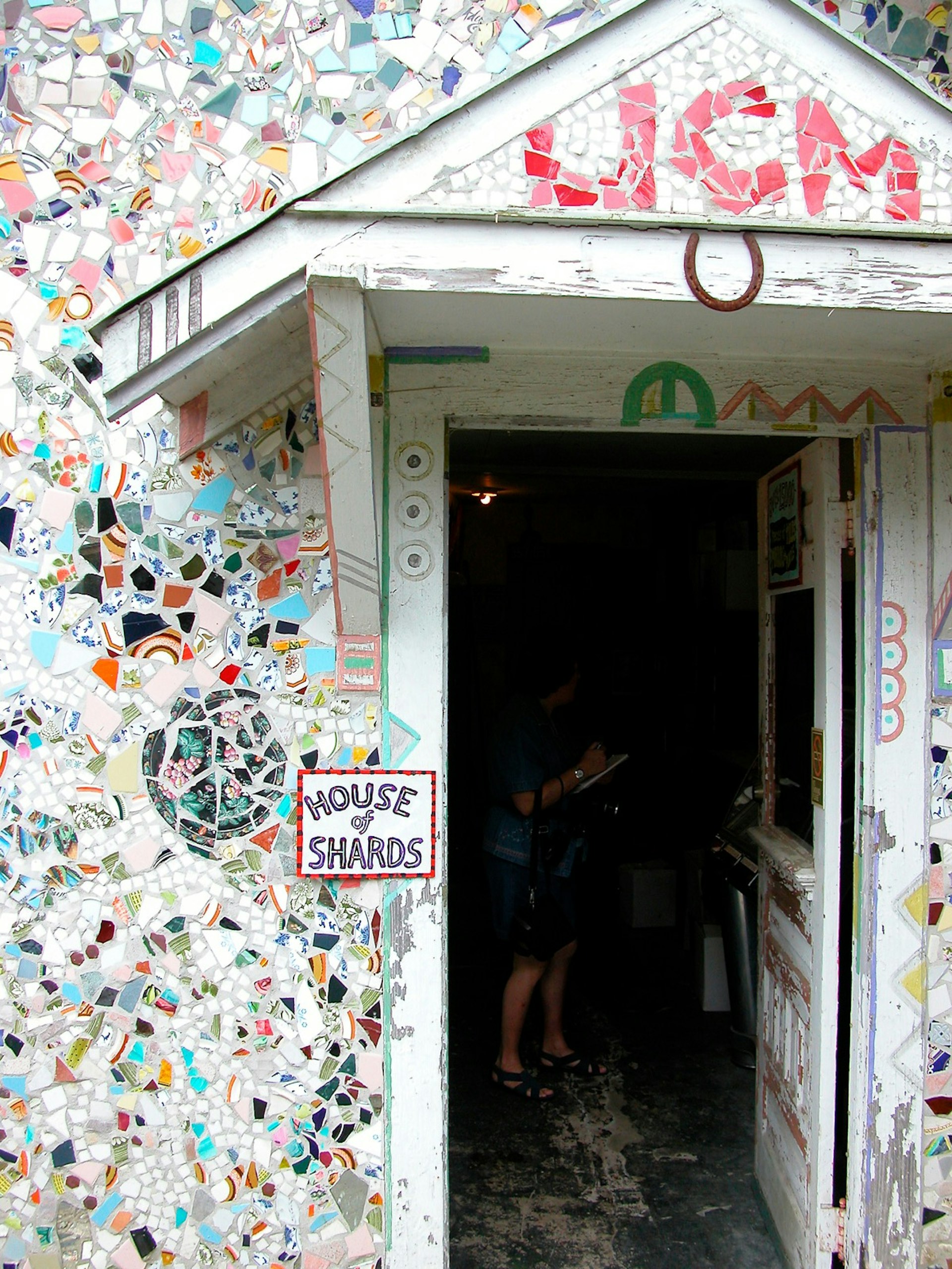 A white house covered with colorful pieces of glass. There's a sign that says 'House of Shards' right next to the door. Louisiana is filled with quirky spots. 