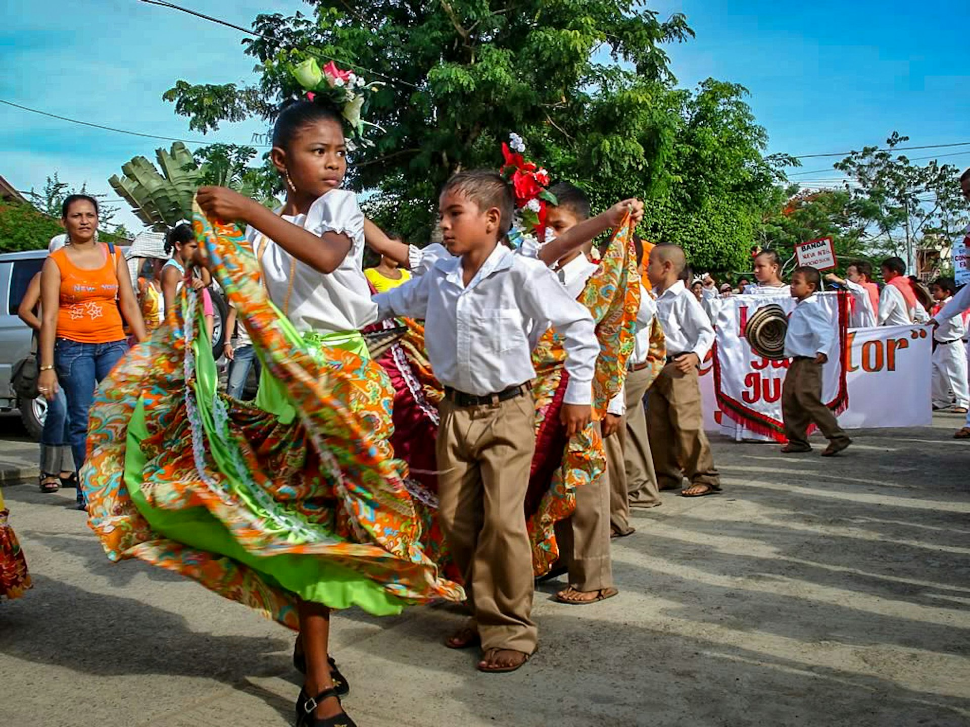 Young girls dressed in colorful skirts and young boys in a white shirt and khakis dance to porro
