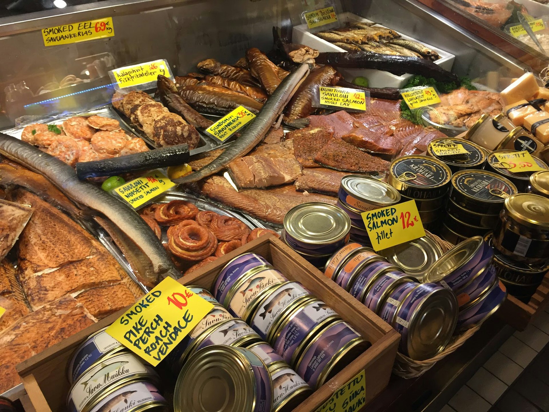 A glass case displaying tins of smoked salmon and a variety of market fish