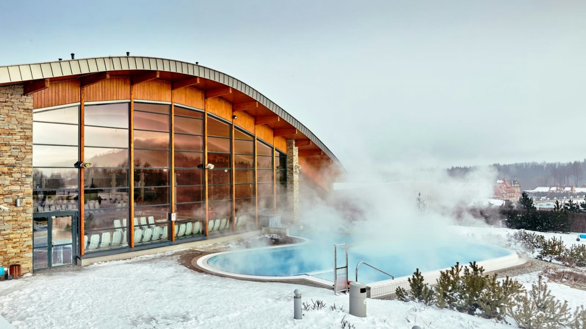 Terma Bania's outdoor thermal pool steaming while surrounded by snow at dusk
