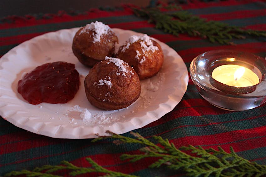 Three delicious æbleskiver – a traditional festive Danish treat – on a plate beside a candle © Caroline Hadamitzky / Lonely Planet