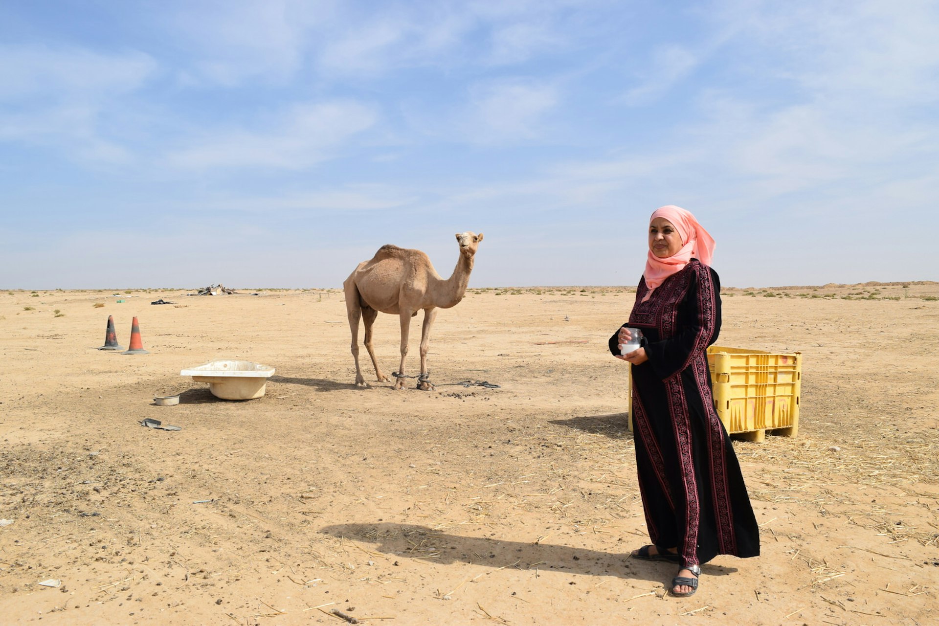 Mariam Abu Rkeek, founder of Desert Daughter, holds a jar of camel milk with a camel in the background in the Negev desert, Israel