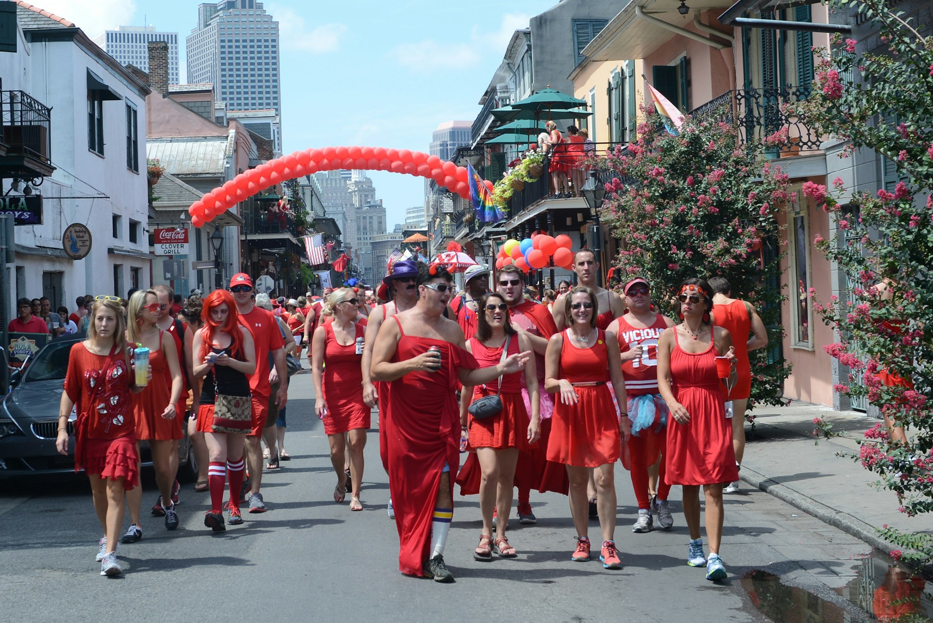 A group of men and women all wearing red dresses walk down the streets of New Orleans.  