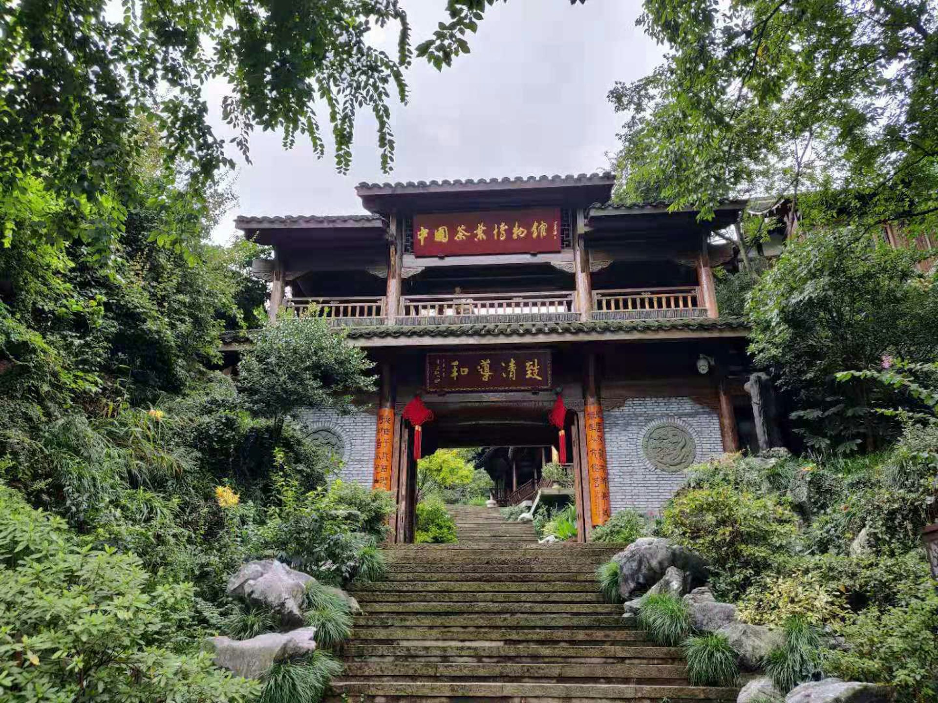 A traditional Chinese gate with flying eaves at the top of some steps surrounded by rocks and trees