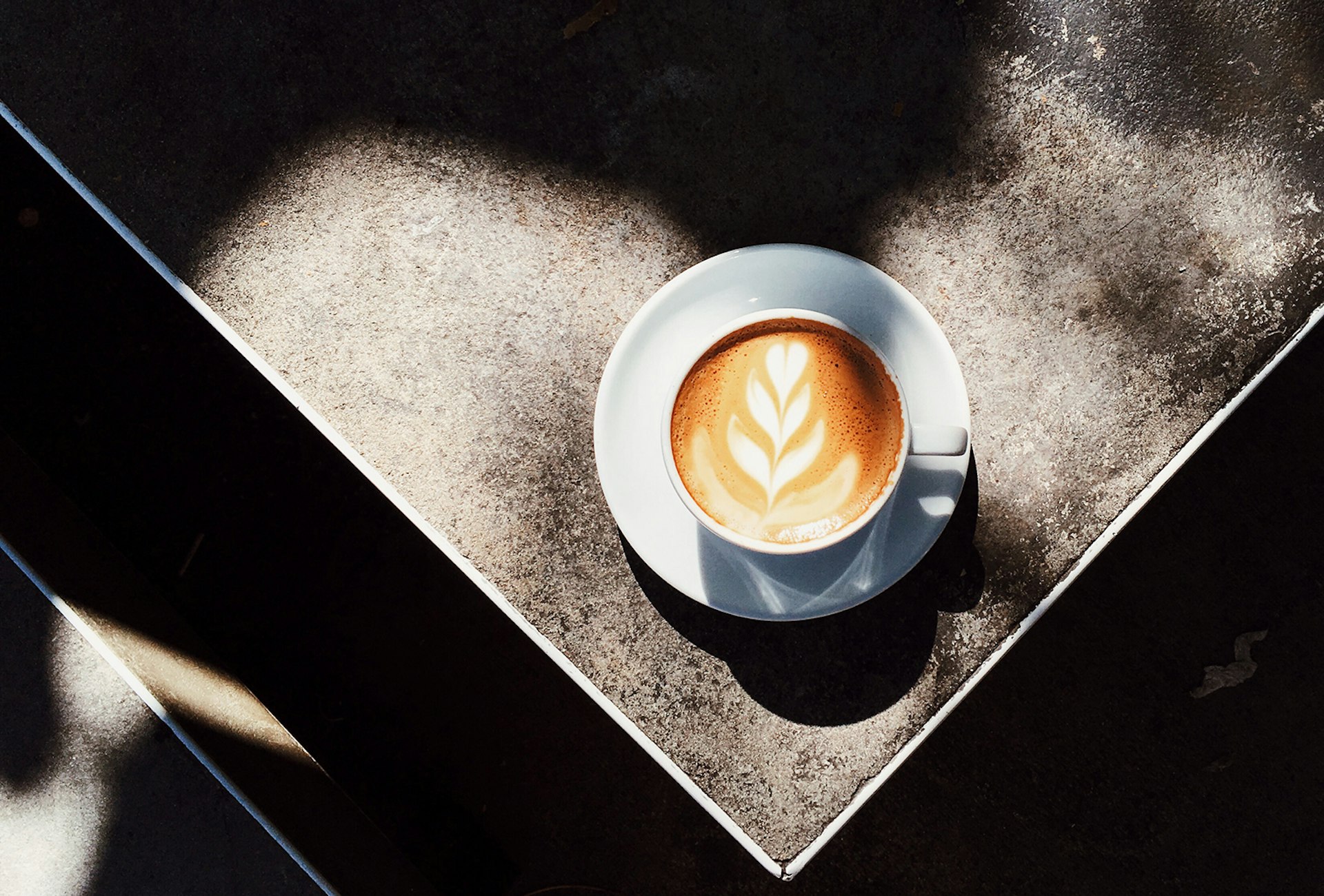 A latte sits on a concrete table in a spot of sunshine