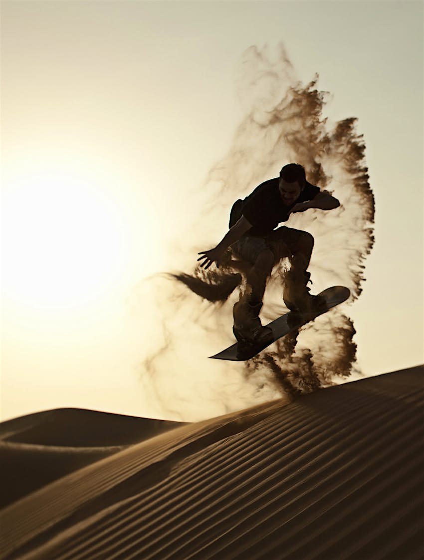 Young man sandboards down a dune in the desert