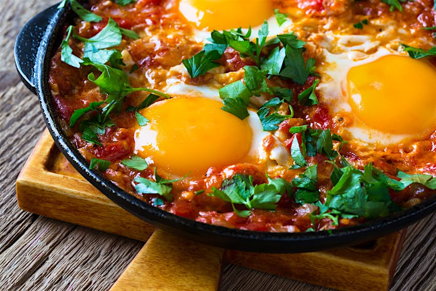 Bowl of shakshuka, a homemade egg dish with tomato sauce served in cast iron pan