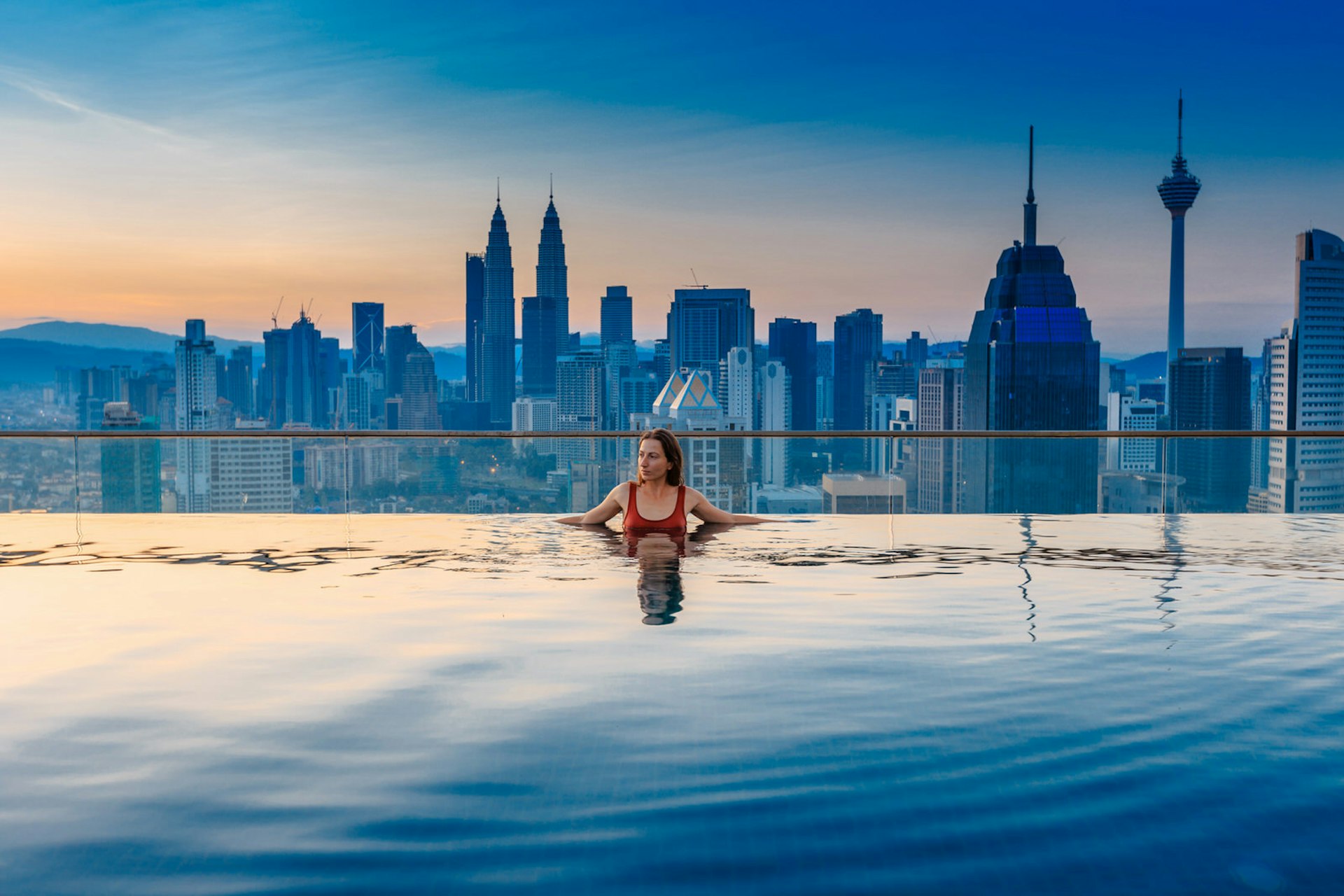 A swimmer relaxes in an infinity pool, backdropped by the Kuala Lumpur skyline.