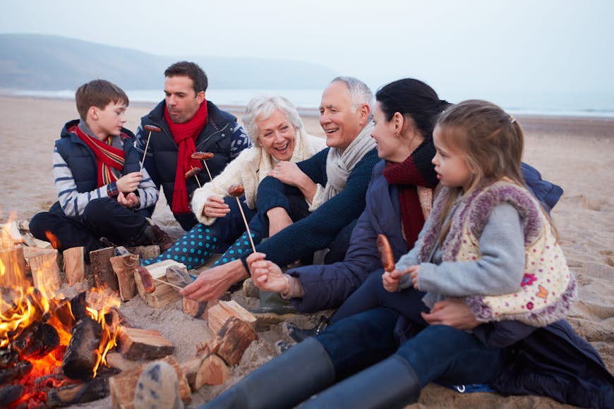 A group of grandchildren, parents and grandparents enjoy a beach BBQ on an autumnal day