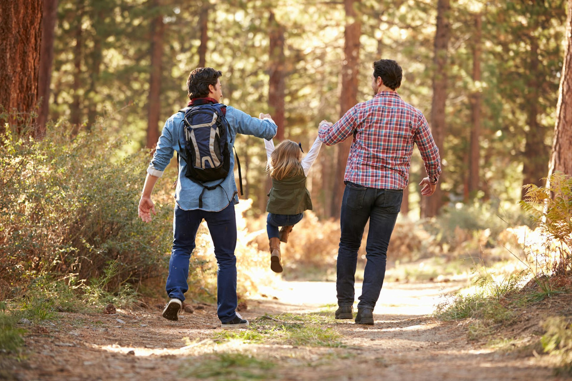 A pair of dads take their daughter on a walk through the forest during an affordable family vacation