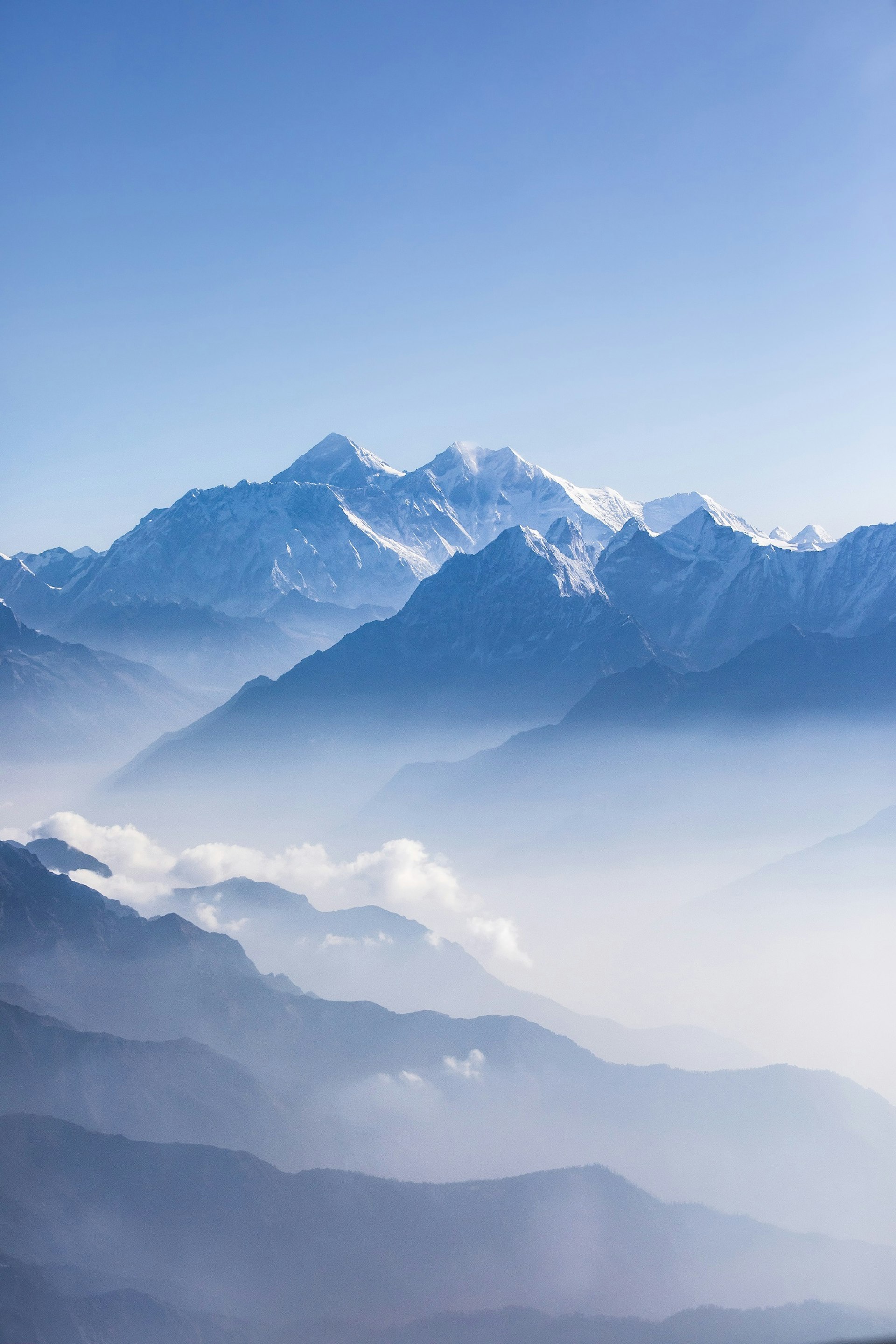 A stunning mountain range with clouds smothering some peaks: Mount Everest and other Himalayan peaks on a sunny day.