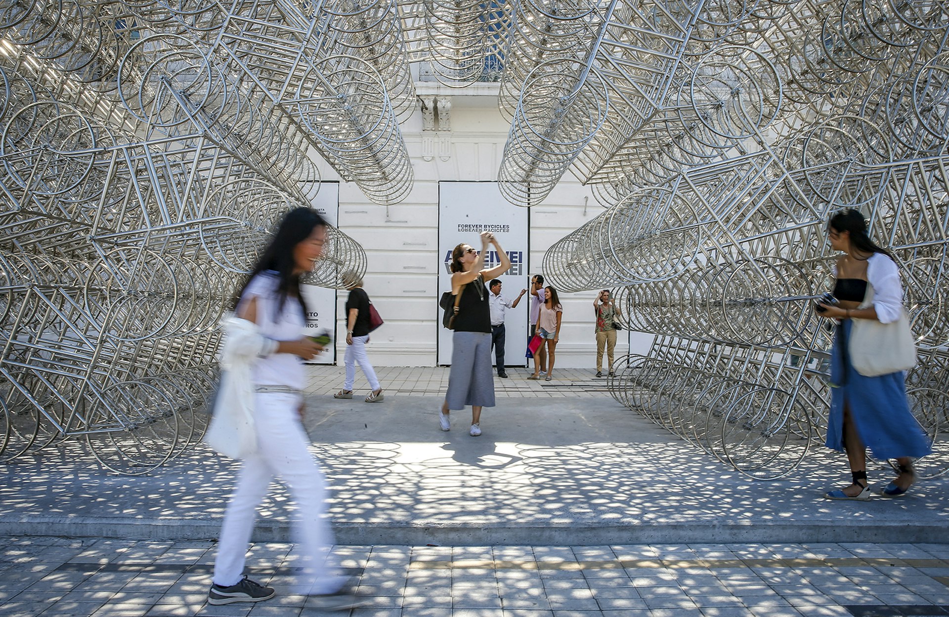 People walk past and take pictures of an Ai Wei Wei art installation, a tunnel made out of dozens of silver metal bicycle sculptures