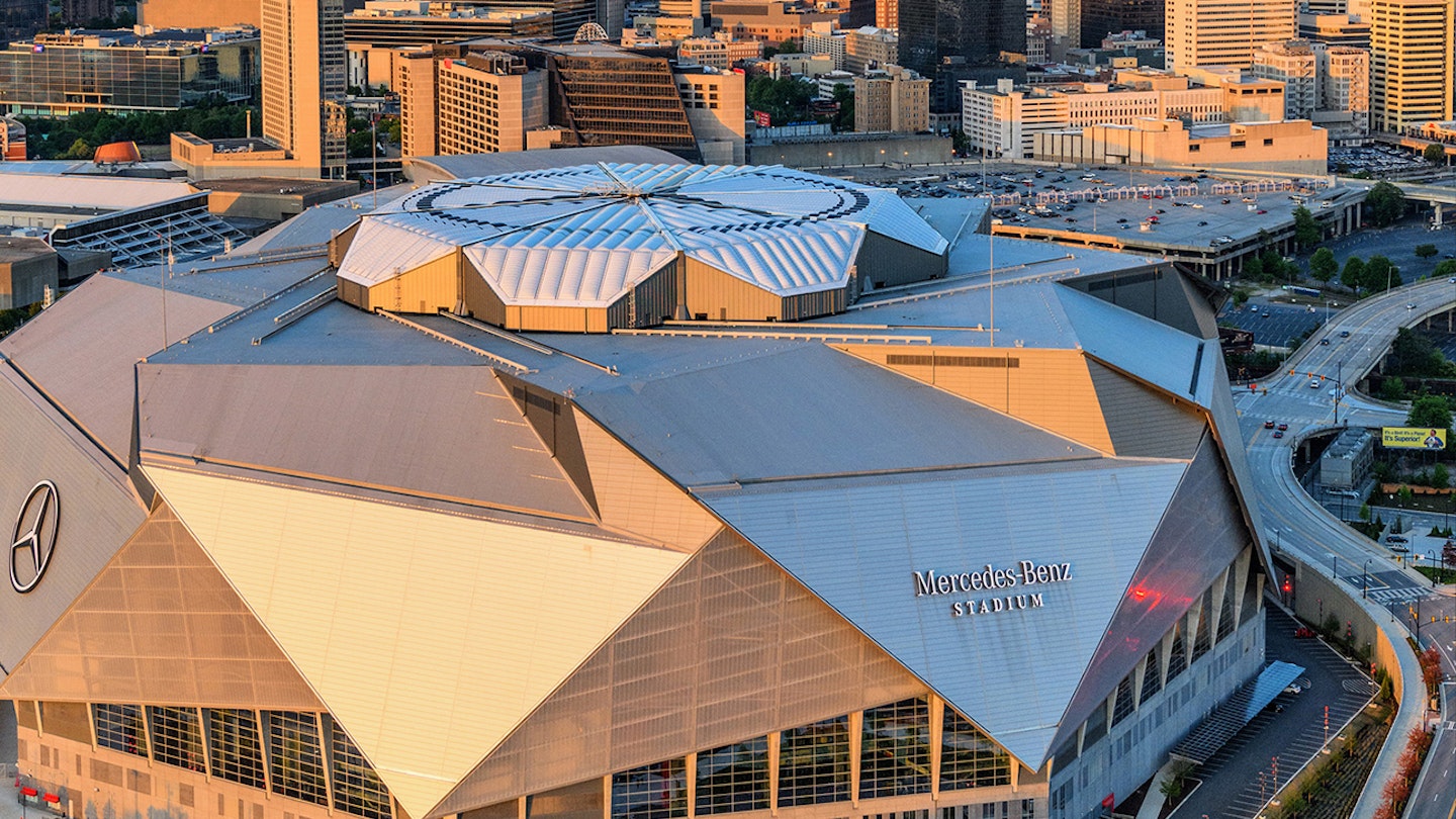 Sun glints off the multifaceted dome of the new Mercedes Benz Stadium in Atlanta, with the skyline behind it at sunset