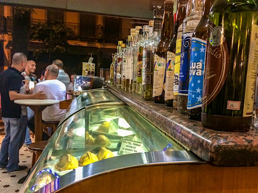 A side view of a food display case with pastries inside and alcohol bottles lining the top