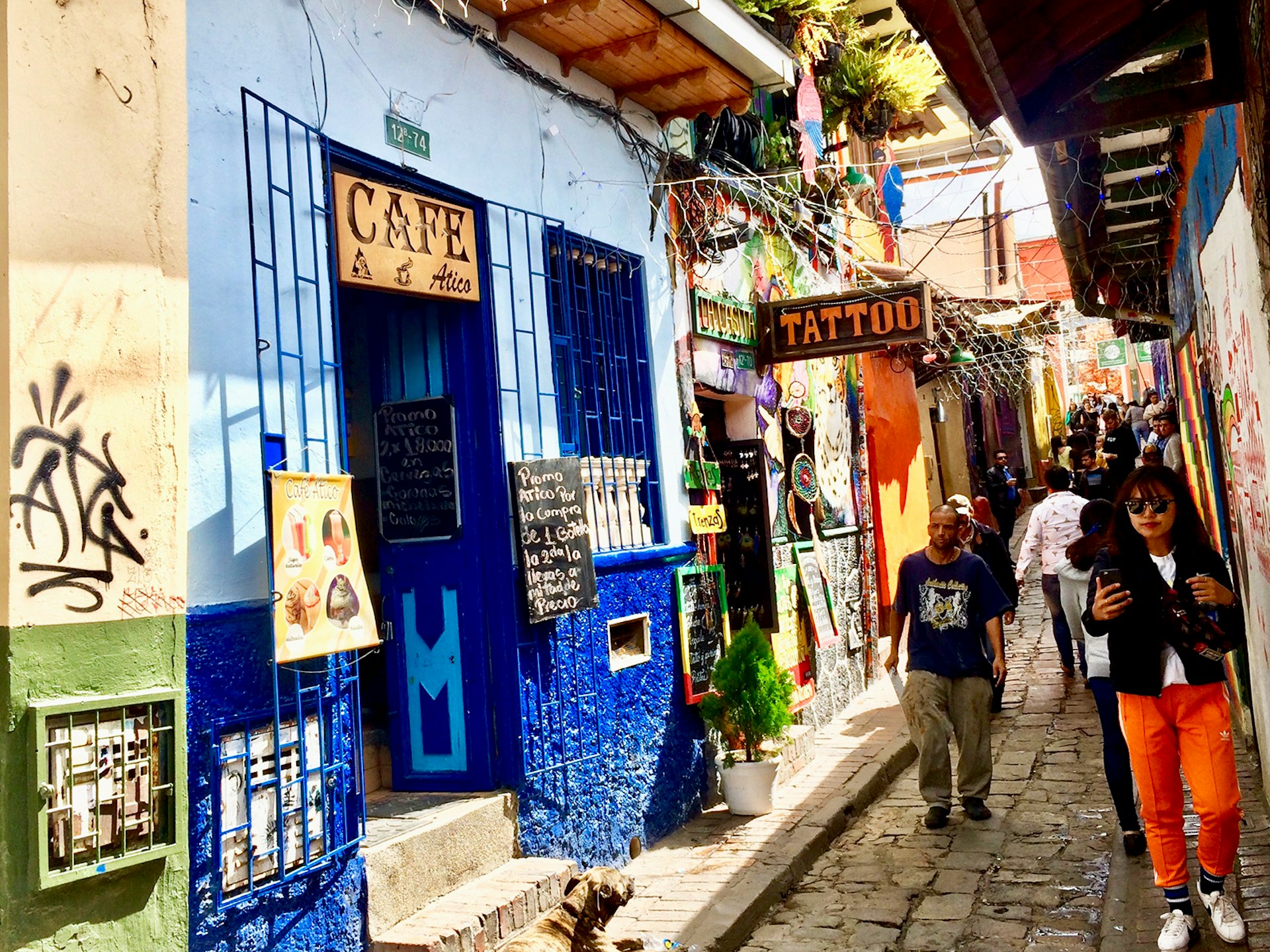 People walk down a narrow cobblestoned streets with colorfully painted shops on either side