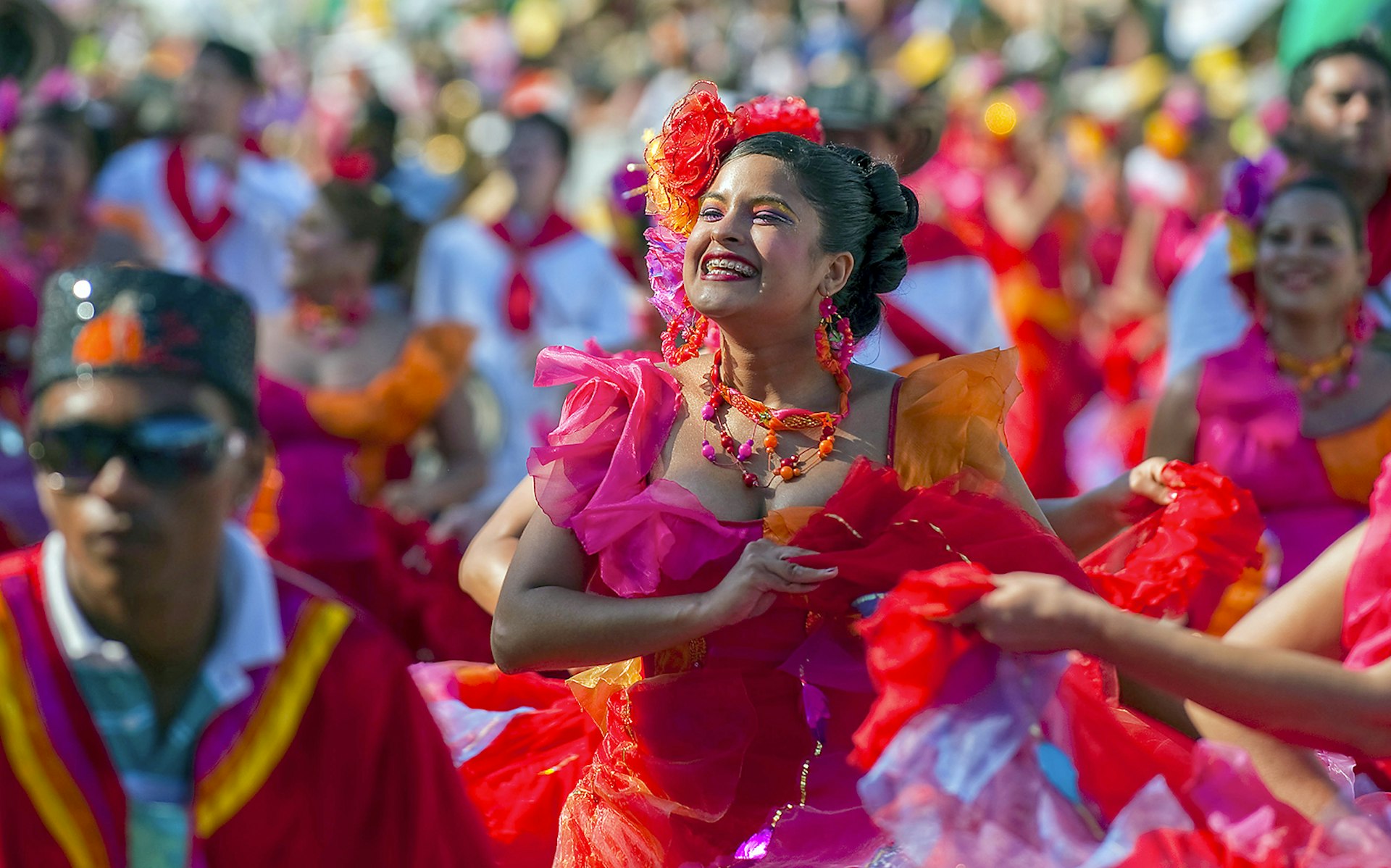 A woman wearing a frilly pink and orange dress smiles at the crowd while dancing