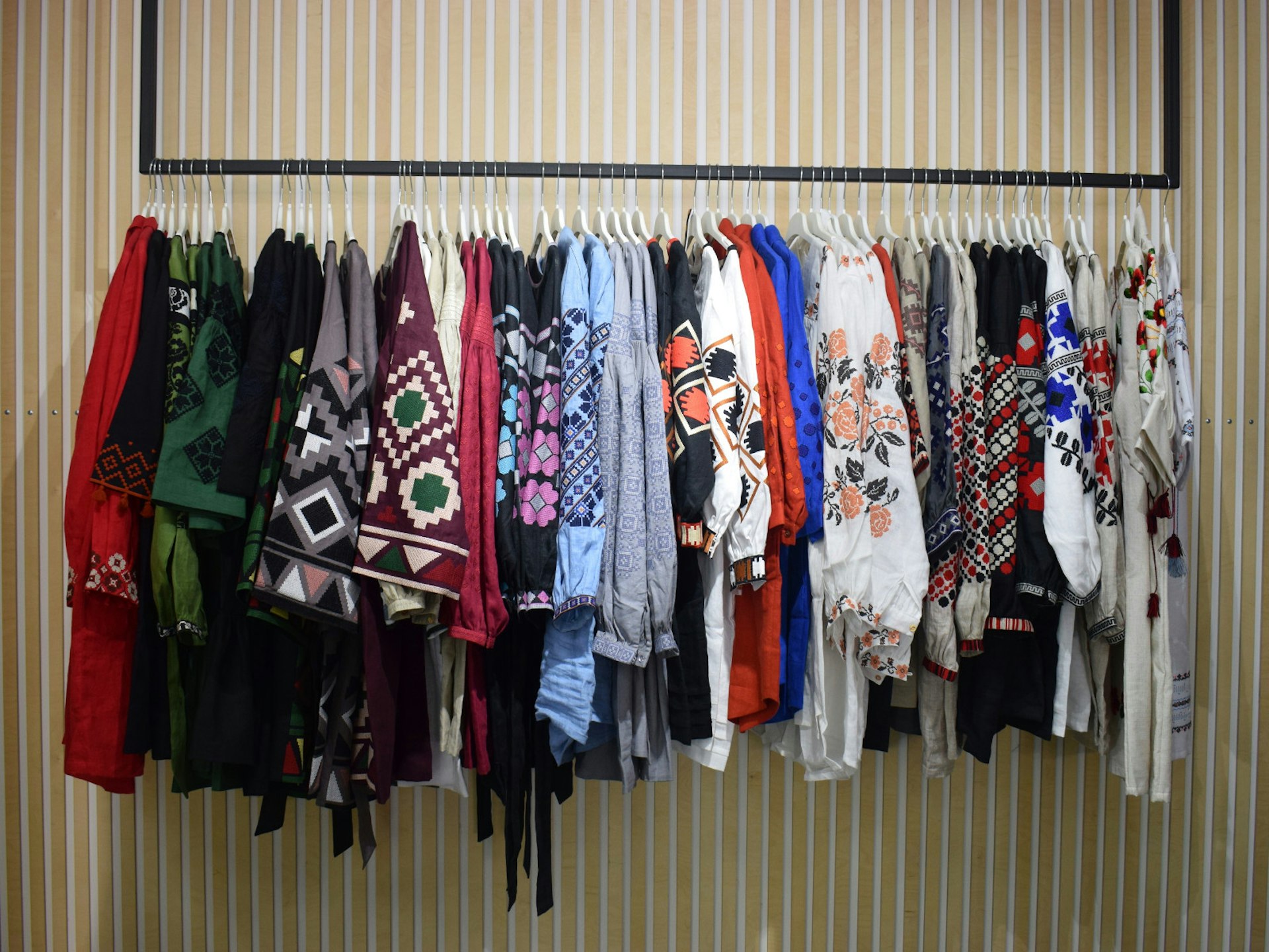 A colourful selection of Ukrainian embroidered shirts hang against a striped wall in Etnodim boutique © Pavlo Fedykovych / Lonely Planet