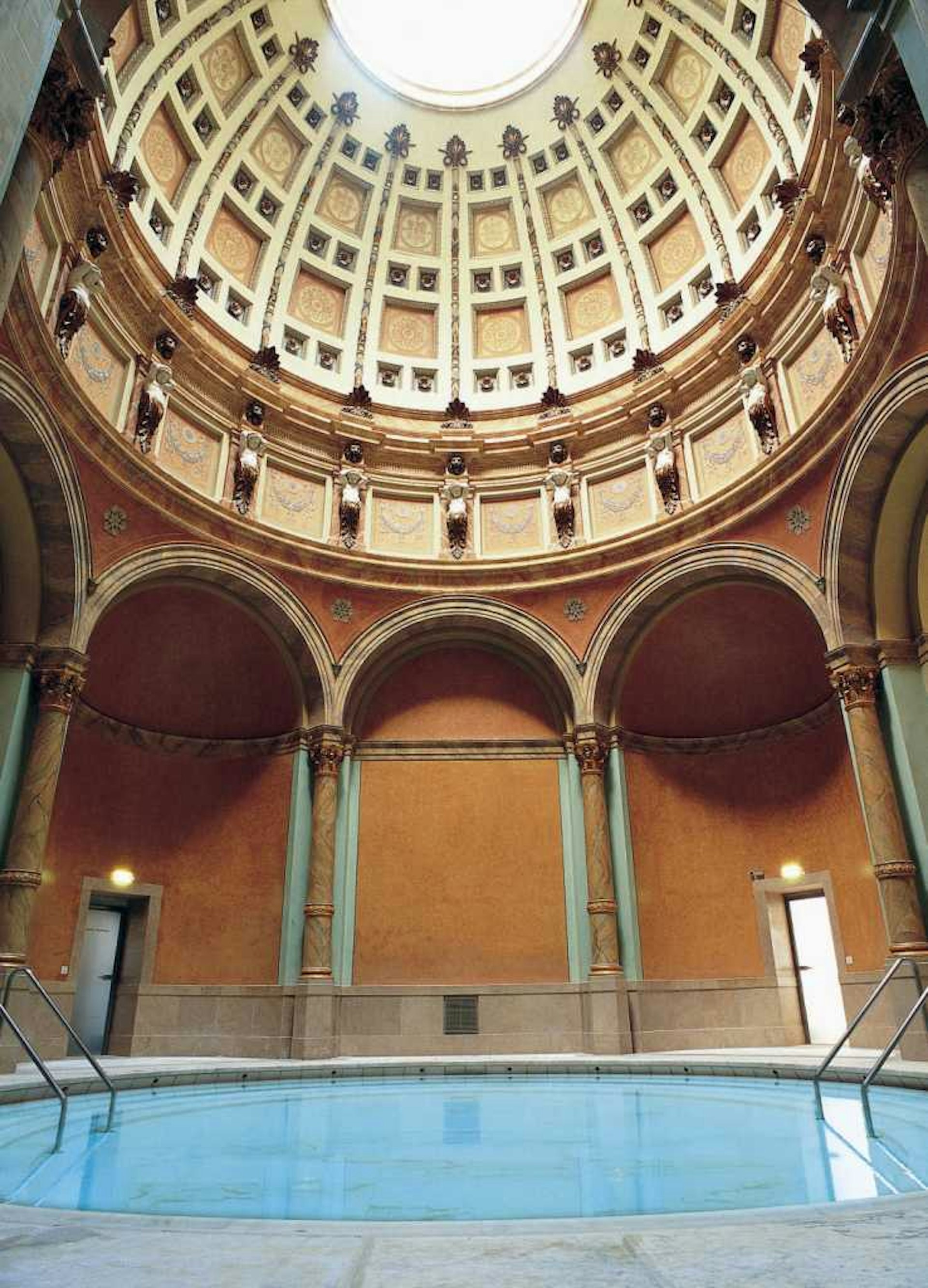 A circular pool sits below a high-domed ceiling with intricate details in the Friedrichsbad 