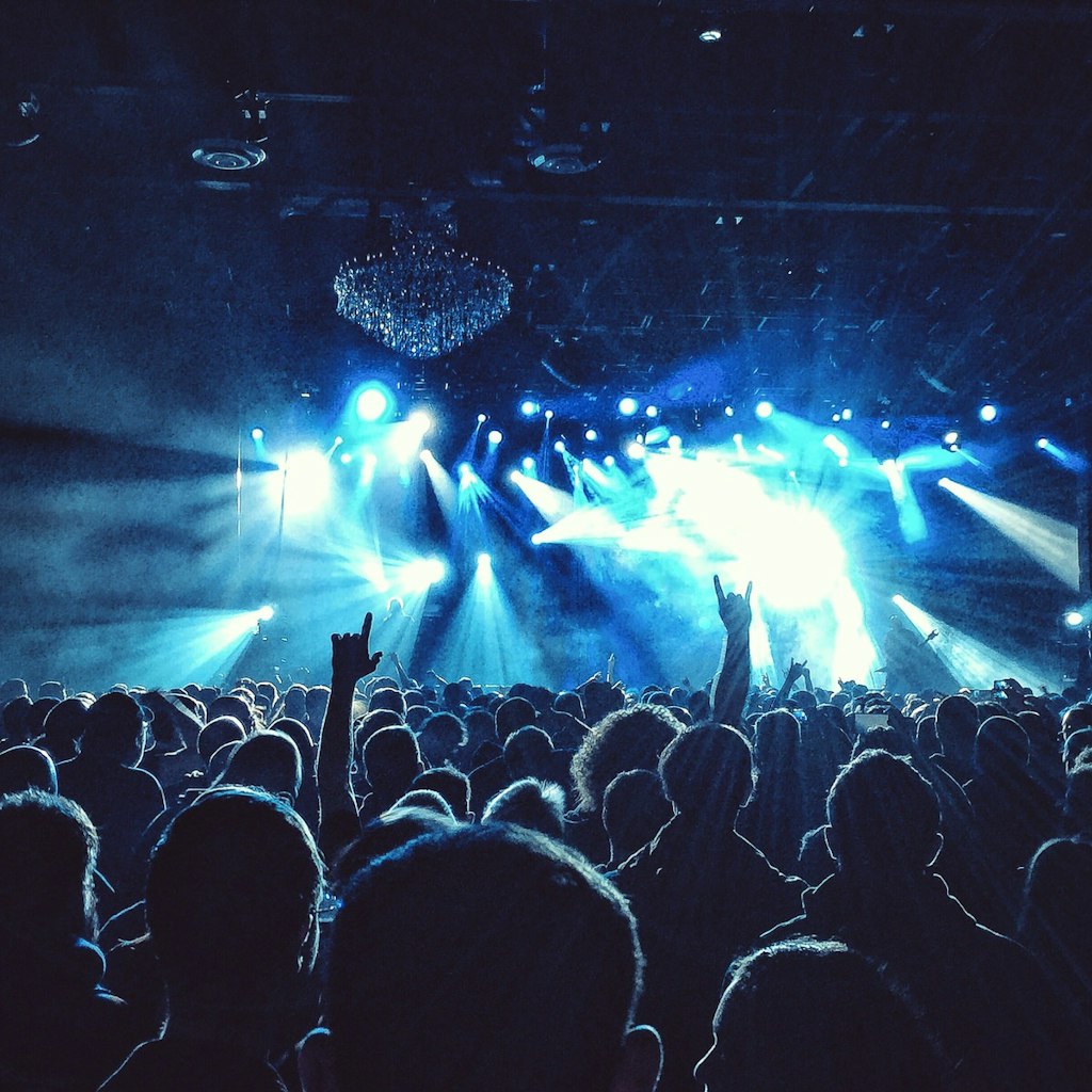 A sea of spectators are in shadow in front of a stage in Philadelphia, USA, where indigo and white lights flash from the venue's ceiling