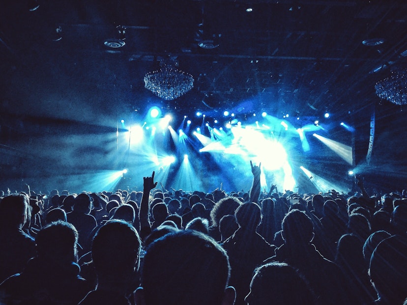 A sea of spectators are in shadow in front of a stage in Philadelphia, USA, where indigo and white lights flash from the venue's ceiling
