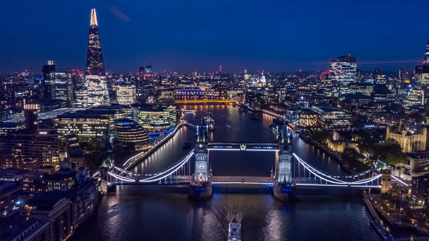 A night-time aerial view of London's skyline shoiwng Tower Bridge and the Shard.
