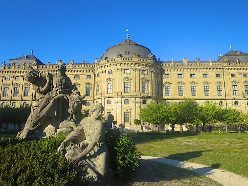 Features - IMG_1220-188140a1e617 Würzburg Residenz, an impressive palace in Austrian/German baroque style, also inspired by Versailles. The palace lawn is adorned with trees and sculptures. its yellow facade contrasts with the bright blue sky