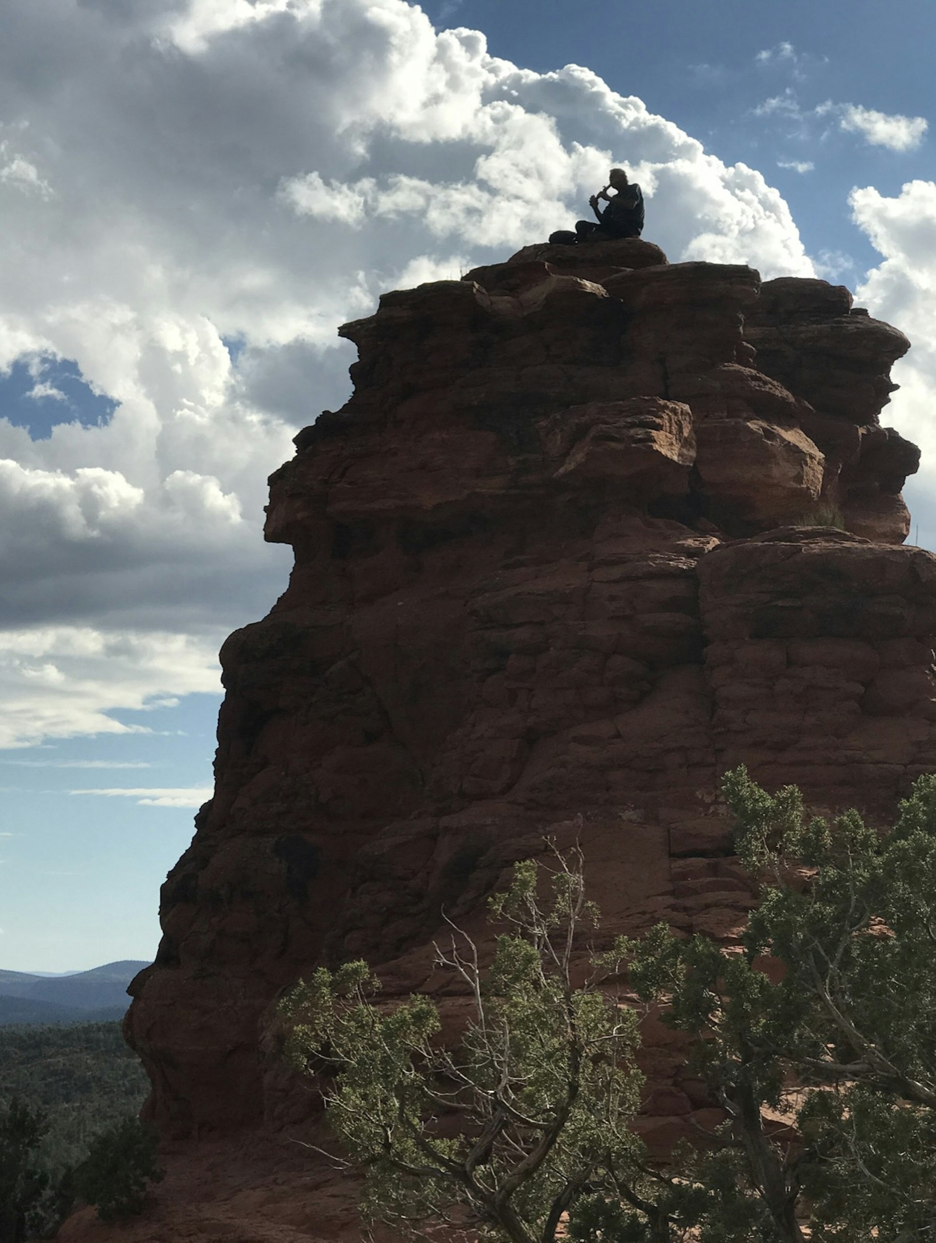 A man sits on top of a rock formation as clouds fill the sky around him