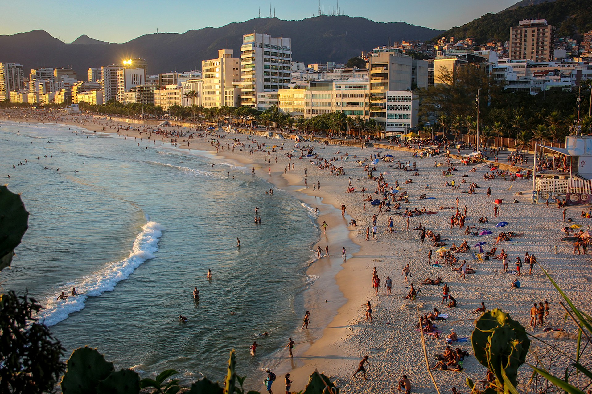 An overhead image of people on a curved beach at sunset, with city buildings lining the sand