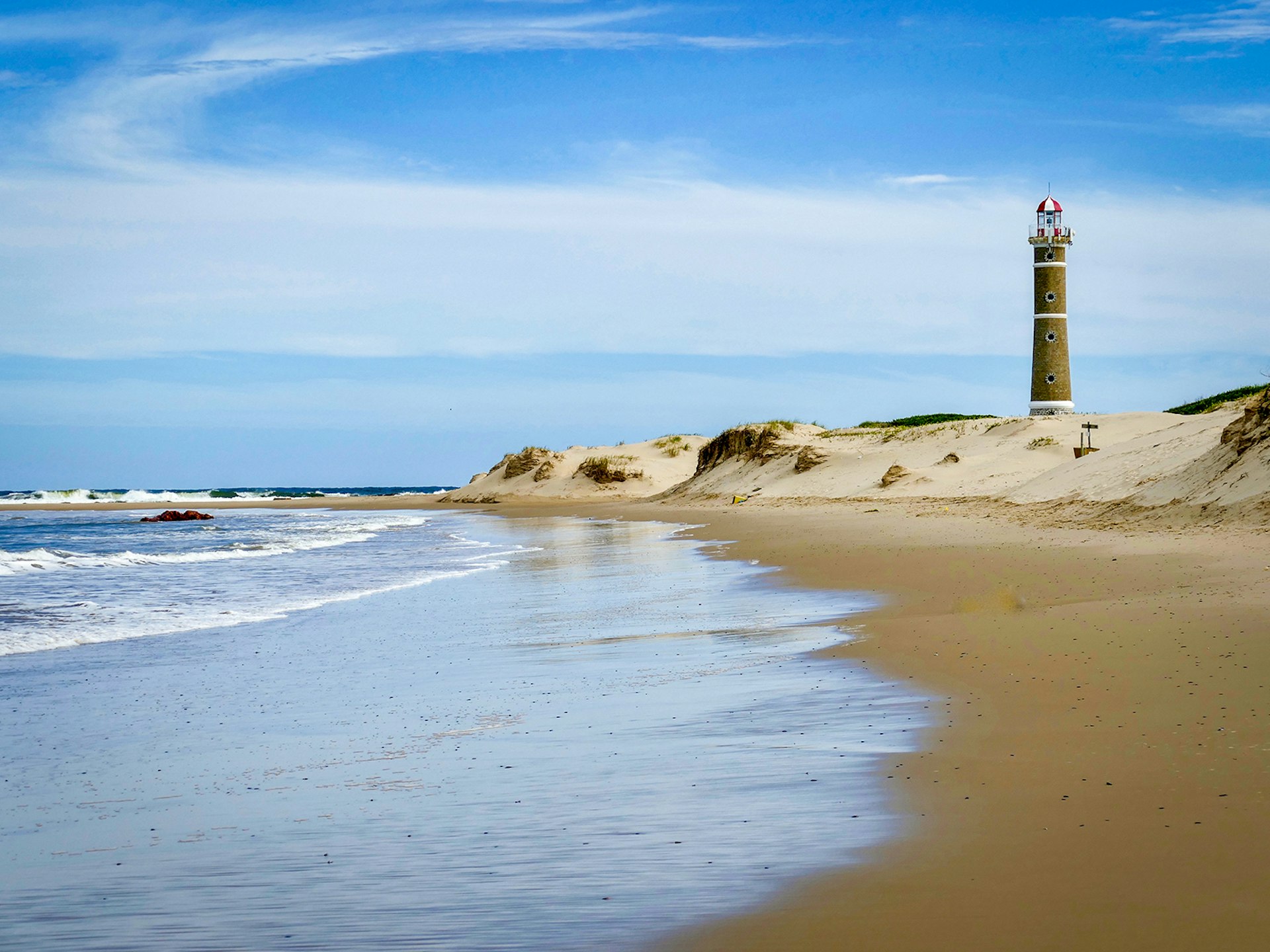 An empty beach with gold sand on a sunny day, with a lighthouse in the background on the right
