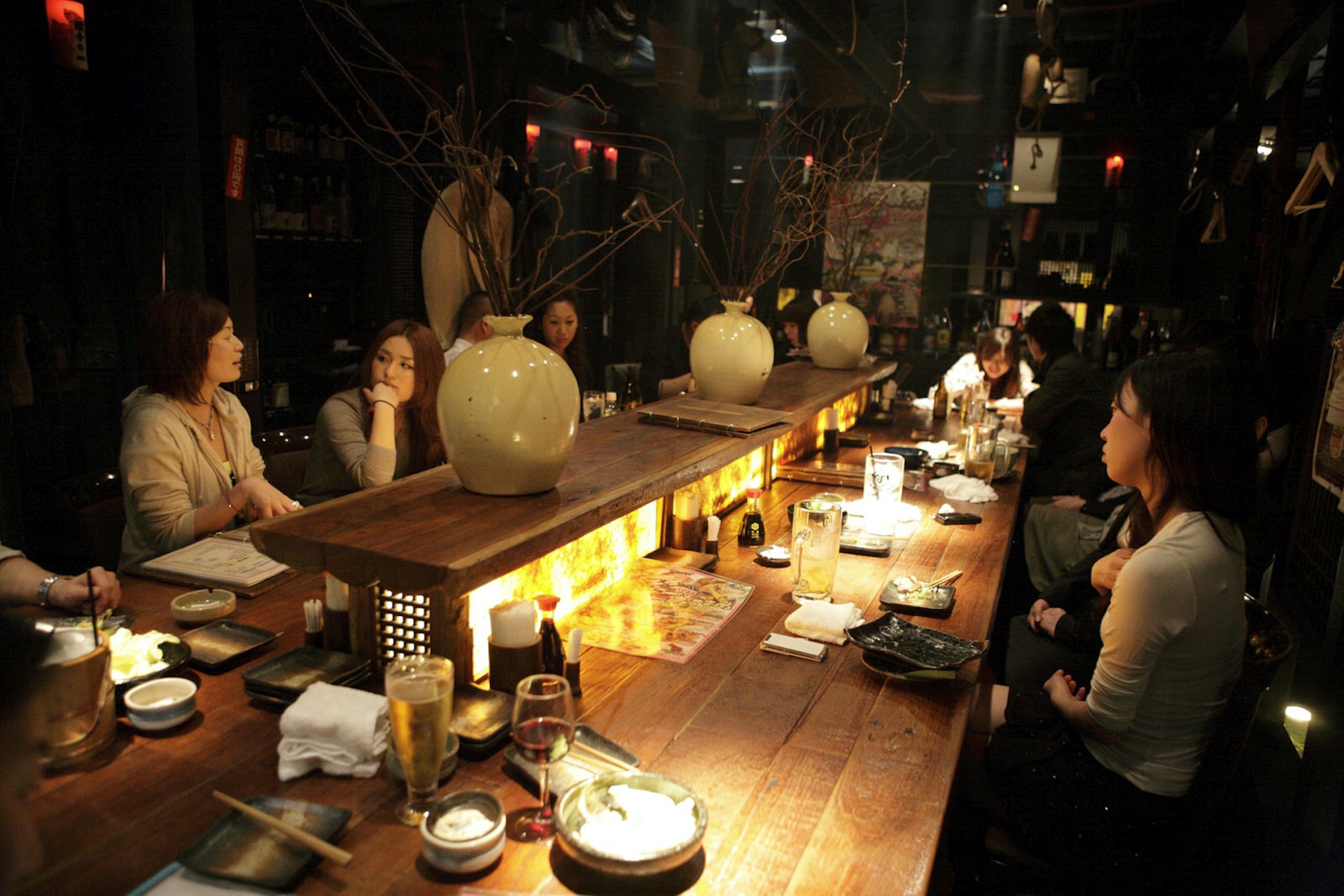 A long wooden table in a downlit Tokyo restaurant, with local diners conversing over pretty ceramic plates