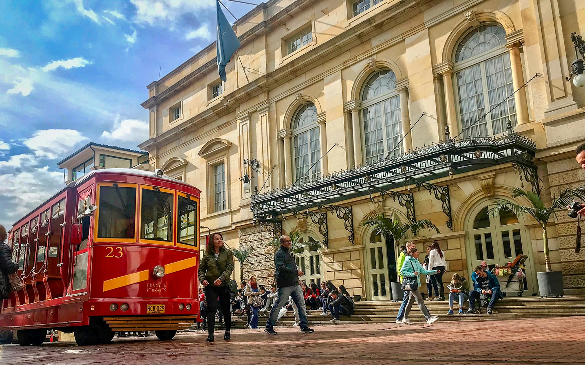 A red tram passes in front of the golden stone facade of the Teatro Colón in Bogota on a sunny day © Jacqui de Klerk / Lonely Planet