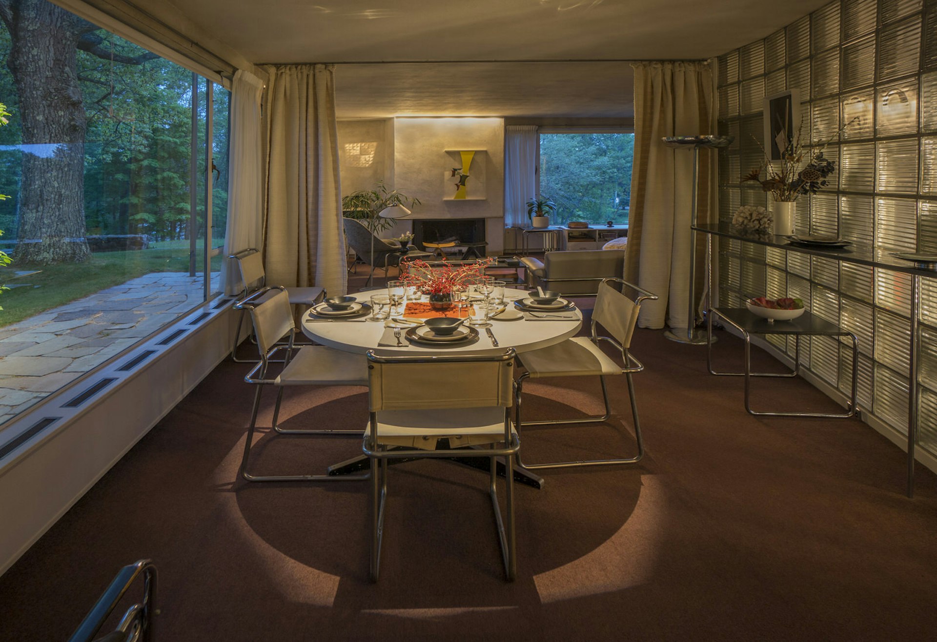 A table and chairs with metallic legs, metal-and-glass feature wall and a huge window give this downlit dining room in Gropius House a modernist vibe